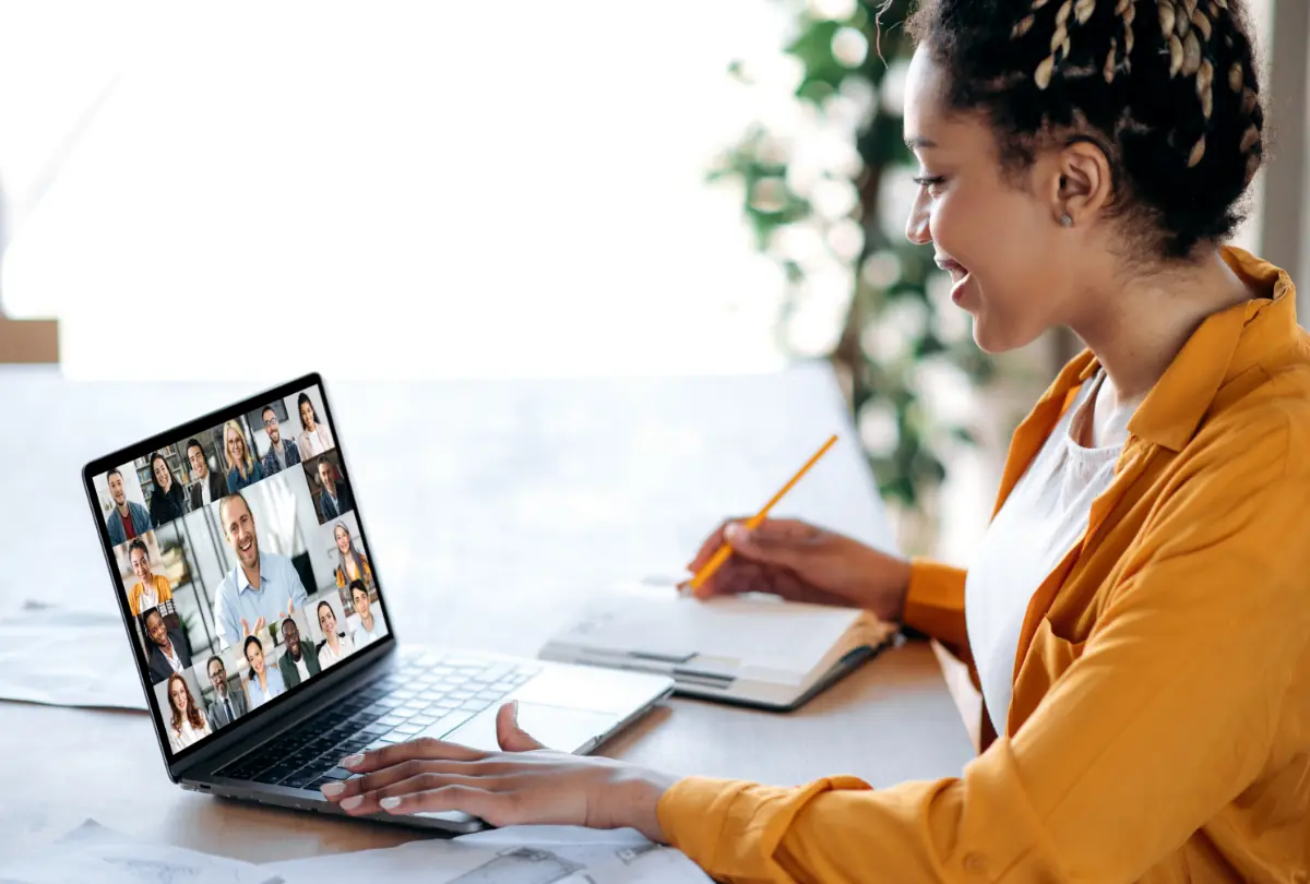 Maigsing pagpupulong, kumperensiya. Isang Aprikanong Amerikanong babaeng manager ang nakikipag-ugnayan sa business team sa panahon ng video call, nakikinig sa financial webinar, at kumukuha ng mga tala